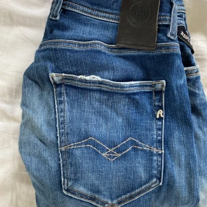 Replay Grover jeans blå slim fit - Säljer ett par Replay Grover jeans i blå tvätt med snygga slitningar och kontrastsömmar. Jeansen har klassisk femficksdesign, smal passform och normal midja. Materialet är stretchigt denim för extra komfort. Perfekta för dig som gillar en modern och stilren look.