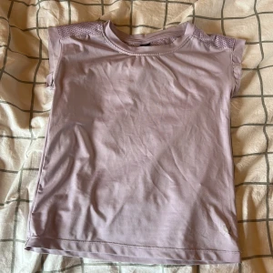 Ljuslila träningstopp från SOC - Säljer en superfin ljuslila träningstopp köpt på stadium med märket SOC i storlek 134-140 som även passar mig som har stl 146/152. Toppen har meshdetaljer över axlarna för extra ventilation och är ärmlös med rund halsringning. Perfekt för dig som vill ha en enkel och snygg topp till träningen. Säljer pga att den inte kommer till användning.