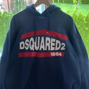 Blå DSQUARED2 hoodie med tryck - Snygg blå hoodie från DSQUARED2 med stort vitt och rött logotryck på bröstet och huva med snörning. Perfekt för dig som gillar streetwear och vill sticka ut med en ikonisk look. Mjuk bomullskänsla och relaxed fit.