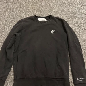 Svart Calvin Klein sweatshirt - Svart sweatshirt från Calvin Klein Jeans med broderad cK-logga på bröstet och Calvin Klein Jeans-tryck på ärmen. Klassisk rund halsringning och långa ärmar. Perfekt basic med stilren look. Xs men passar även S