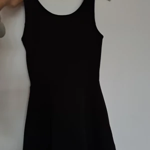 Svart kort klänning från H&M Divided - En svart, ärmlös kortklänning från H&M, Divided i storlek 34. Klänningen har rund halsringning och en enkel, stilren design med lätt utställd kjol. Perfekt för dig som gillar minimalistisk och klassisk stil.