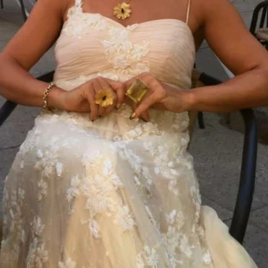 Aftonklänning  - Drömmig långklänning i champagnefärg med tunna axelband och vackra broderade spetsblommor över hela klänningen. Den har en romantisk, flowy passform och transparent lager som ger en lyxig känsla. Perfekt för bal eller sommarens stora event.Storleken är justerbar eftersom den har remmar baktill