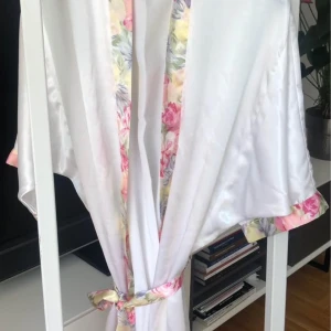 Badrock med blommigt band  - Superfin badrock  i satin med blommiga detaljer längs kanterna och bältet. Lätt och glansigt material, perfekt för en chill sommarlook eller när du vill känna dig extra lyxig hemma.