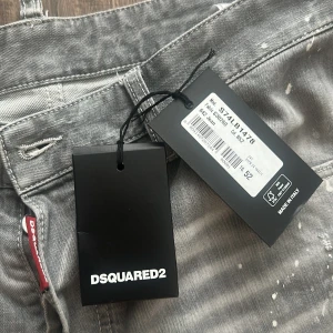 Grå Dsquared2 jeans med färgstänk - Snygga grå jeans från Dsquared2 med coola slitningar och vita färgstänk för en edgy vibe. Klassisk femficksmodell i bomull med rak passform och diskret Dsquared2-logga vid fickan. Perfekta för dig som vill sticka ut med en streetinspirerad look. Äkta jeans, kvitto finns med!! Original pris, just nu högstabud på 1995kr