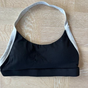 Svart och vit sportig linnetopp - En stilren svart linnetopp med vita kanter och bred resår nedtill. Perfekt för träning eller en chill look. Axelbandslös design med enkel och sportig känsla. Snygg att matcha med höga byxor eller shorts.