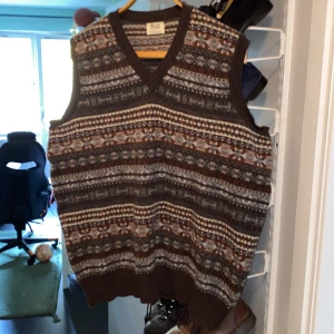 Brun mönstrad ullväst William Lockie - Säljer en brun och grå stickad väst från William Lockie i 100% lammull. Västen har klassiskt mönster med inslag av beige och vitt, v-ringning och ribbad nederkant. Perfekt för lager-på-lager och skotsk vintagekänsla. Nypris ligger runt 2000