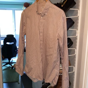 Rutig skjorta Stenströms Fitted Body 43 - Säljer en snygg rutig skjorta från Stenströms i modellen Fitted Body. Skjortan är vit med bruna och vinröda rutor, har lång ärm och klassisk krage med knappar. Tillverkad i mjuk och lyxig bomull. Perfekt för dig som gillar stilrena och tidlösa plagg.