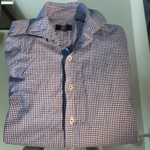 Blårutig skjorta från Boggi Milano - Snygg blårutig skjorta från Boggi Milano i storlek S. Skjortan har klassisk krage, vita knappar och lång ärm. Tillverkad i mjuk bomull och har ett stilrent rutmönster i blått och vitt. Perfekt för dig som gillar en clean och tidlös look.