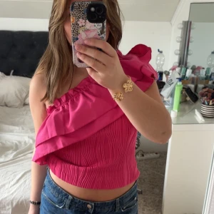 Rosa one shoulder volangtop - Vet inte vart den är ifrån, köpte den på arkivet. Säljer en snygg rosa one shoulder topp med volangdetalj och ribbad. Perfekt för dig som vill ha något färgstarkt och trendigt i garderoben.