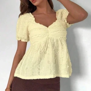 Ljusgul blus med puffärm - Supersöt ljusgul blus med korta puffärmar och v-ringad hals. Blusen har en volangig, luftig passform och struktur i tyget som ger en romantisk känsla. Perfekt för vår och sommar när du vill ha något lätt och fräscht.