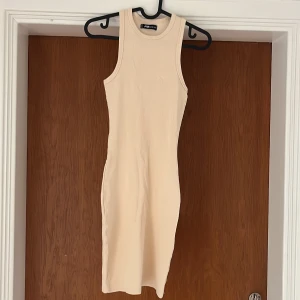 Beige/gul ribbad ärmlös klänning - Säljer en tight, ribbad kortklänning i beige/gul färg från FB sister. Klänningen är formfitting i storlek M. Klänningen är aldrig använd och är i jätte bra skick.