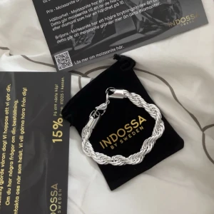 Flätat silverarmband från Indossa - Snyggt och stilrent armband från Indossa i flätad design. Armbandet är 10mm kedja, 21cm lång. Säljer då den inte passade. Helt oanvänd endast testat snabbt