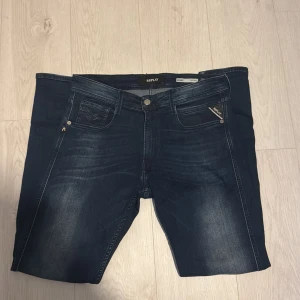 Mörkblå Replay jeans med tvättade detaljer - Snygga mörkblå jeans från Replay med klassisk femficksdesign och coola tvättade detaljer framtill och baktill. Jeansen har en läderpatch med Replay-logga bak i midjan och smal passform. Perfekta för dig som gillar stilrena och trendiga jeans Bronny sitter likt anbass. Storlek 32/32