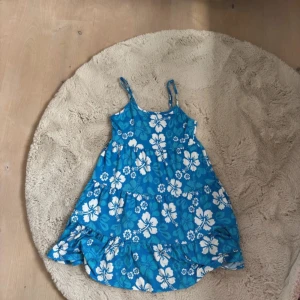 Miniklänning - Supersöt blå klänning med vita blommor från House Brand. Den har smala axelband, volangkant nertill och ett flowy fall. Perfekt för varma dagar och ger riktiga sommarvibbar. Mjuk och lätt i materialet, sitter bekvämt och är enkel att styla. Liten fläck i nedre kant