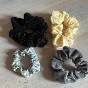 Fyra scrunchies i olika färger och mönster - Säljer fyra scrunchies: en svart i ribbad manchester, en gul och vit rutig i bomull, en ljusblå med blommigt mönster och en grå i mjuk sammet. Perfekta som armband eller hårsnoddar för att ge din look en extra touch.                                 Kontakta mig om du har någon fråga ❤️
