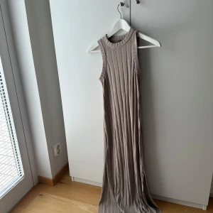 Beige ribbad långklänning H&M XS - Supersnygg beige långklänning från H&M i ribbat material. Ärmlös modell med rund halsringning och figurnära passform. Perfekt för dig som gillar stilrena och bekväma plagg med lite edge.