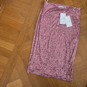 Rosa paljettkjol från Vila - Glittrig rosa kjol från Vila, täckt med paljetter för en extra festlig look. Modellen är rak och slutar ovanför knäna. Perfekt för dig som vill sticka ut med en snygg och trendig stil. Färgen heter Misty Rose och kjolen har en mjuk insida. Aldrig använd! 