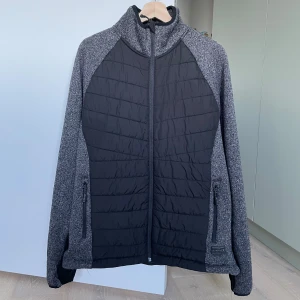 Svart och grå pufferjacka Bluewear XL - Säljer en svart och grå pufferjacka från Bluewear i storlek XL. Jackan har quiltad framsida och rygg, hel dragkedja och två fickor med dragkedja. Tillverkad i 100% polyester och har en sportig, clean look som passar perfekt till höst och vinter.