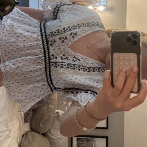 Vit blus med blått mönster från zara - Supersöt vit blus med blått småmönster och svarta broderade detaljer. Blusen har v-ringning, volang nertill och korta puffärmar. Perfekt för vår och sommar, lätt och luftig i bomull.