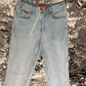 Ljusblå  jeans från Butter - Ljusblå jeans från Butter med relaxed fit och snörning i midjan. Klassisk femficksmodell med broderad detalj på bakfickan och läderpatch med logga. Perfekta för en avslappnad stil.