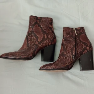 Bruna boots med ormmönster - Säljer ett par bruna boots med ormmönster från Zara Woman. Skorna har hög klack, rund tå och dragkedja på sidan. Perfekta för dig som vill sticka ut med en trendig look.