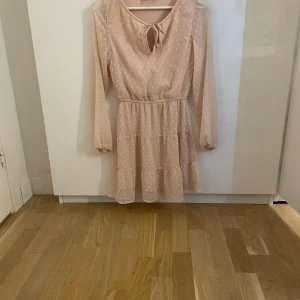 Ljusrosa prickig klänning med volang - Söt ljusrosa klänning med vita prickar och volangdetaljer. Klänningen har lång ärm. Tillverkad i ett lätt och luftigt material, perfekt för vår och sommar. Aldrig andvänd 