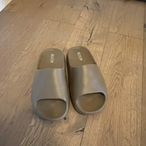 Beige slip-in sandaler från Nelly.com - Säljer ett par stilrena beige sandaler från Nelly.com. Modellen har öppen tå och platt sula, perfekt för varma dagar. Tillverkade i syntetmaterial och har en minimalistisk design som passar till många outfits.