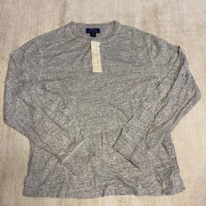 Grå långärmad tröja från Polo Ralph Lauren - Säljer en grå långärmad tröja från Polo Ralph Lauren med tre knappar vid halsen och broderad logga nertill. Tröjan är i mjuk bomull och har en klassisk, avslappnad passform. Perfekt för en stilren vardagslook.