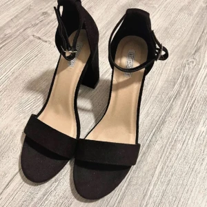 Svarta klackskor med ankelrem - Säljer ett par stilrena svarta klackskor från Bershka med öppen tå och bred klack. Skorna har en enkel rem över tårna och justerbar ankelrem. Perfekta för dig som vill ha en klassisk och bekväm klacksko. Aldrig använda, bara testade