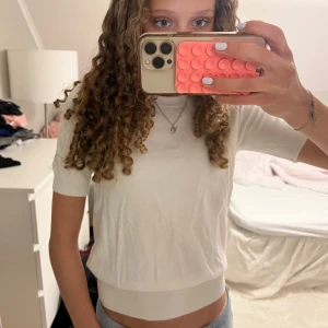 Vit kortärmad stickad tröja - Säljer en vit, kortärmad stickad tröja med rund hals och ribbade kanter. Tröjan har en enkel och stilren design som passar perfekt till jeans eller kjol. Perfekt för vår och sommar!