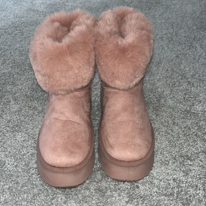 Rosa fluffiga boots - Säljer ett par supermysiga rosa boots med fluffig päls runt skaftet och platt sula. Perfekta för kyliga dagar och ger en trendig look till vinterns outfits.