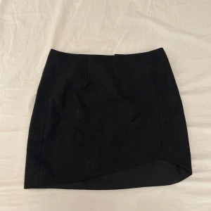 Svart kjol från & Other Stories - En svart kortkjol från & Other Stories med enkel och stilren design. Kjolen har en lätt asymmetrisk nederkant och är tillverkad i ett mjukt material som känns bekvämt. Perfekt att matcha med olika toppar för en trendig look.