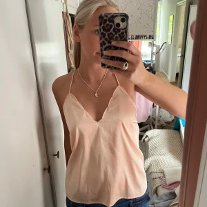 Ljusrosa linnetopp med tunna axelband - Säljer en ljusrosa linnetopp med tunna axelband och djup v-ringning. Toppen har en enkel och stilren design med slät yta och öppen rygg. Perfekt för varma dagar eller att styla lager på lager.