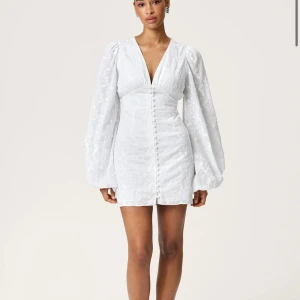 Adoore kortklänning med puffärmar - Snygg vit kortklänning med djup v-ringning och långa puffärmar. Klänningen har markerad midja och knappar framtill, vilket ger en elegant och trendig look. Perfekt för sommarens alla tillfällen.