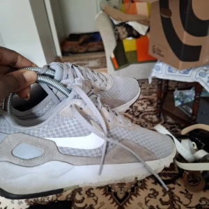 Gråa Nike sneakers med vit sula och vit swoosh - Säljer ett par gråa Nike sneakers med vit sula och vit swoosh på sidan. Skorna har mesh-överdel och detaljer i mocka, samt snörning framtill. Perfekta för vardagsbruk och har en sportig look.