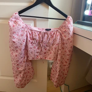 Rosa blommig korsettopp från Boohoo - Supersöt rosa korsettopp från Boohoo med blommigt mönster och ballongärmar. Toppen har knytning framtill. Perfekt nu inför sommaren😊 storlek 36, kan nog passa 38 oxå😊 aldrig använd☺️