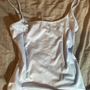 Blå  linnetopp med smala axelband - Säljer en enkel och stilren vit linnetopp med smala axelband. Perfekt att matcha med jeans eller kjol för en fräsch look. Toppen är i mjukt material och har en rak passform.