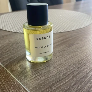 ESSNCE  Parfum tobacco vanille doupe  - Parfymflaska med gul vätska från ESSNCE, doften heter Bacco Le Doux. Flaskan är rund med svart lock och vit etikett med svart text. 50ml och Max använt 10 sprut. Doupe av Tom Ford tobacco vanille. Gillar du Tom Ford så är denna parfym för dig. 