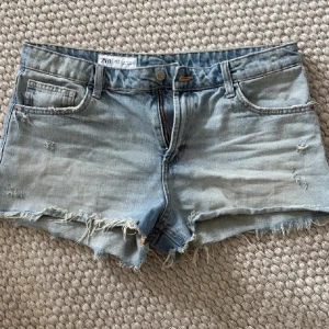 Ljusblå jeansshorts från Zara - Säljer ett par ljusblå jeansshorts från Zara med råa kanter och slitningar. Klassisk femficksmodell med knapp och dragkedja. Perfekta för varma dagar och enkel att matcha med olika toppar.  
