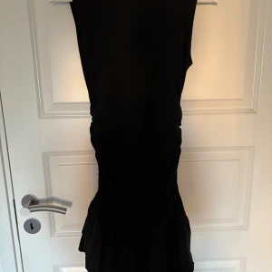 Svart ärmlös klänning med rynkade detaljer - Säljer en svart ärmlös klänning med snygga rynkade detaljer längs sidan och volang nertill. Klänningen har en tight passform💕