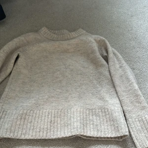 Beige stickad tröja från C - Mysig beige stickad tröja från C med ribbad krage, ärmslut och nederkant. Perfekt för kyligare dagar och enkel att matcha med olika outfits. Klassisk och tidlös design.