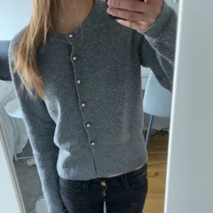 Grå kofta med pärlknappar - Säljer en söt grå kofta med långa ärmar och fina pärlknappar framtill. Koftan är i ett mjukt stickat material och har en klassisk, enkel design som passar till mycket💗