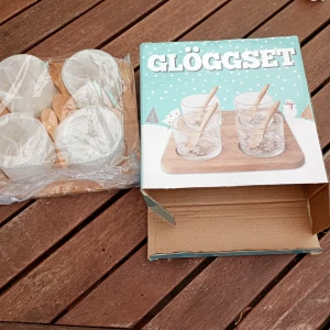 Glöggset med glas och träbrickor - Säljer ett glöggset med fyra genomskinliga glas med vita snöflingor och tillhörande träbrickor. Perfekt för vinterns mysiga stunder. Glasen är runda och har en klassisk form.