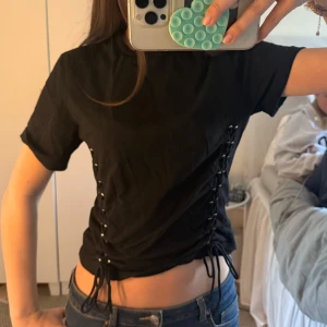 Svart t-shirt med snörning  - Svart croppad t-shirt med korta ärmar och cool snörningsdetalj längs båda sidorna.💗