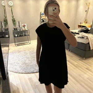 Svart kortklänning med loose passform - Enkel svart kortklänning med loose passform och ärmlös design. Perfekt för dig som gillar minimalistisk stil och vill ha något bekvämt men ändå snyggt. Klänningen har rund halsringning och raka linjer.