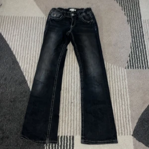 Mörkgrå jeans från Gina Tricot - Säljer ett par mörkgrå jeans från Gina Tricot med vita kontrastsömmar och klassisk femficksdesign. Byxorna har raka ben och normal passform, perfekta för en avslappnad stil. 