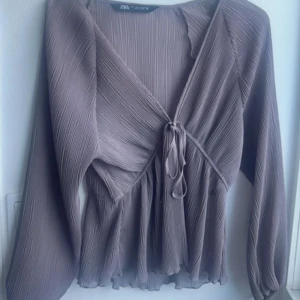 Plisserad blus med knyt från Zara - Så snygg blus från zara!! Andvänd få gånger så super fint skick 💕svårt o avgöra färgen men någonstans mellan grå/ brun, bilden som är tagen är i dagsljus ; så det är den riktiga färgen