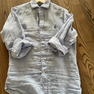 Ljusblå linneskjorta från Ralph Lauren - Säljer en ljusblå långärmad skjorta i linne från Ralph Lauren. Slim fit-modell med  knappar framtill och broderad logga på bröstet. Perfekt för en stilren och avslappnad look till sommaren!
