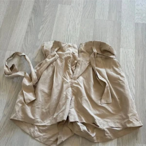 Beigea högmidjade shorts  - Säljer beigea shorts med knytband i midjan. Shortsen har en luftig passform och är perfekt för varma dagar. Enkel och stilren design strl S