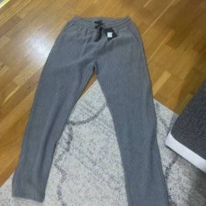 Grå ribbade mjukisbyxor från BOSS - Säljer ett par grå ribbade mjukisbyxor från BOSS med dragsko i midjan. Byxorna har en avslappnad passform och är perfekta för en chill vardagslook. Klassisk design med elastisk midja och mjukt material. Lappen säger xl men de är passar m/s 